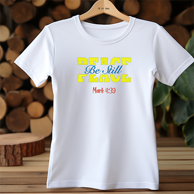 A white t-shirt on a hanger with the words peace be still are embroidered on the front.